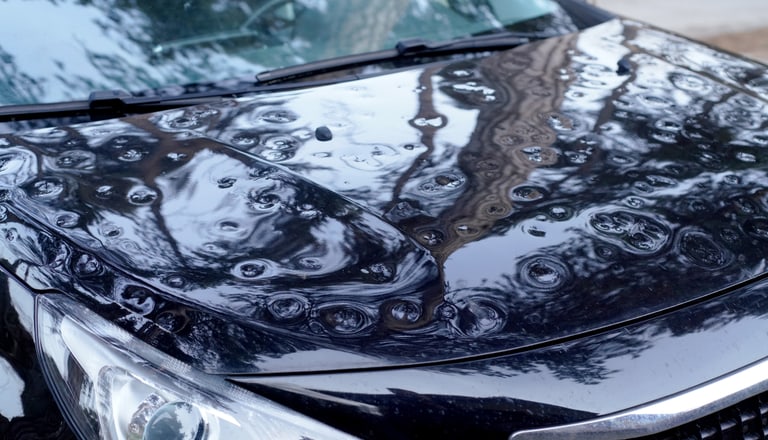 Nahaufnahme der Dellen auf einer schwarzen Motorhaube eines Autos.