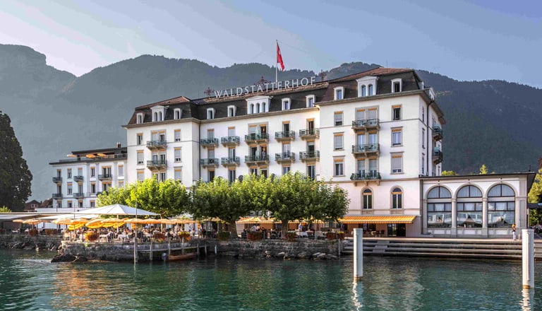 Historisches Hotel am See mit Bergen im Hintergrund.