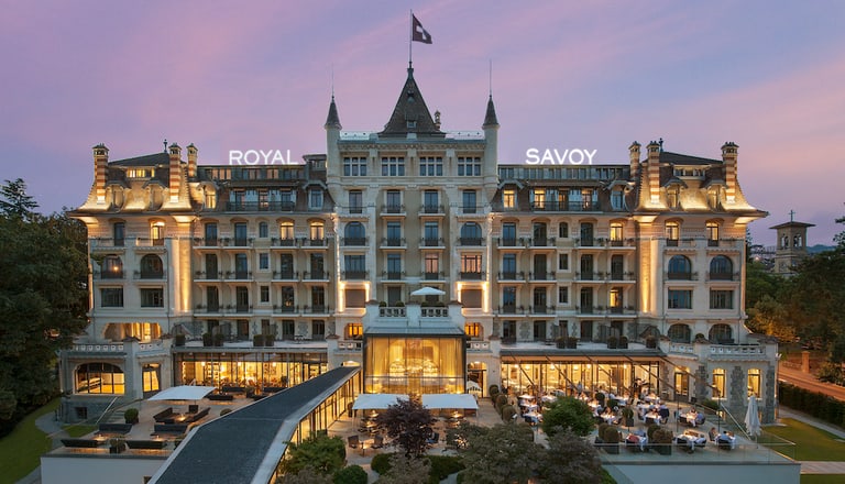 Abendansicht eines grossen, beleuchteten Hotels mit Garten.