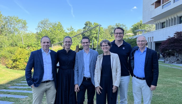 Sechs Personen stehen auf einer Wiese vor einem modernen Gebäude.