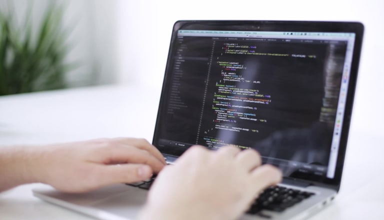 Hände tippen auf einem Laptop mit Code auf dem Bildschirm.