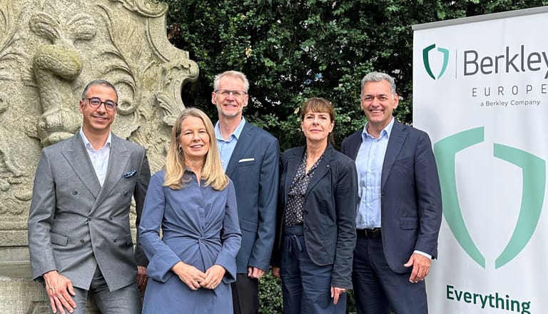 Fünf Personen in Geschäftskleidung neben einem Steindenkmal und einem Berkley Europe Banner.