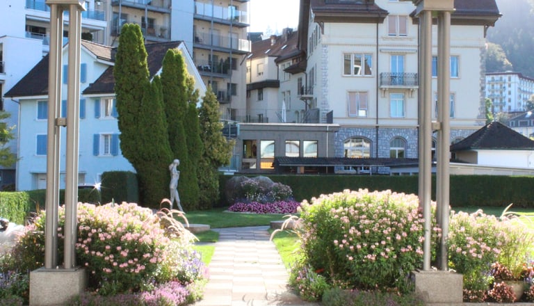 Garten mit Blumen und Statuen vor Gebäuden.