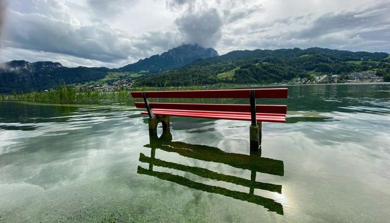 Rote Bank im überfluteten See mit Bergen im Hintergrund.