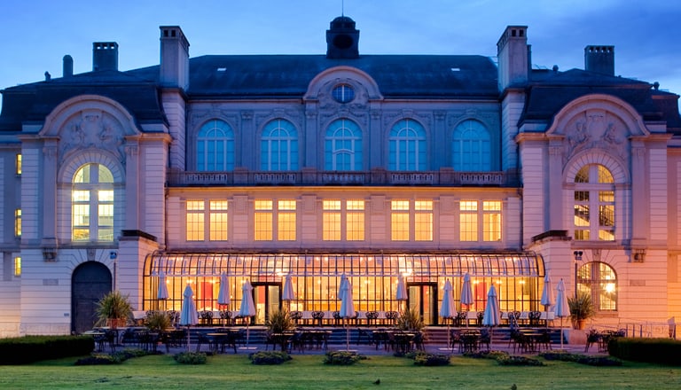 Beleuchtetes Gebäude bei Dämmerung mit Garten im Vordergrund.