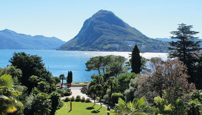 Blick auf See und Berge mit Bäumen im Vordergrund.