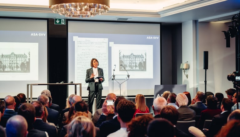 Konferenzredner auf der Bühne mit Publikum im Konferenzraum.