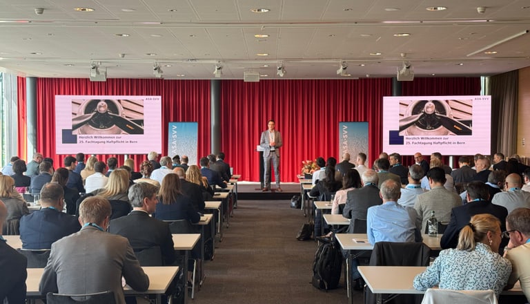 Konferenzraum mit vielen Menschen und einer Person auf der Bühne.