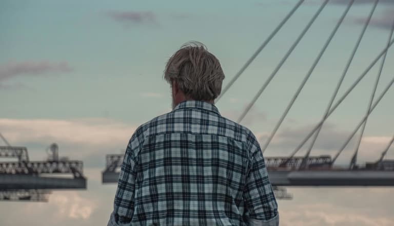 Person mit kariertem Hemd steht vor einer Brücke.