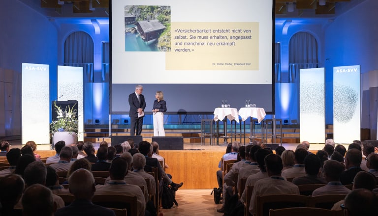 Menschen sitzen in einem Auditorium und schauen zu einer Präsentation auf der Bühne.