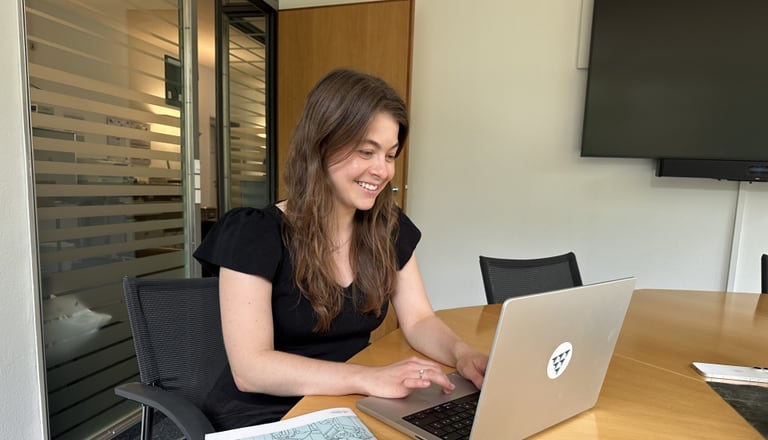 Frau sitzt am Tisch und arbeitet lächelnd an einem Laptop.