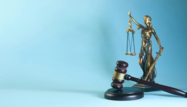 Justitia-Statue mit Waage und Richterhammer vor blauem Hintergrund.
