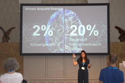 Person hält Vortrag vor Publikum mit Präsentation über Energiebedarf des Gehirns.