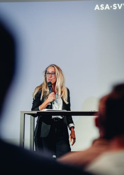 Frau hält Vortrag mit Mikrofon auf einer Bühne.