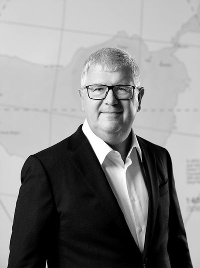 Mann im Anzug mit Brille vor Kartenhintergrund.