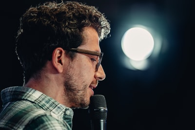 Mann mit Brille spricht in Mikrofon, dunkler Hintergrund mit Lichtschein.