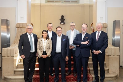 Gruppe von sieben Personen in formeller Kleidung vor einer Treppe.