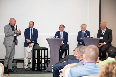 Männer auf einer Podiumsdiskussion auf einer Konferenzbühne.