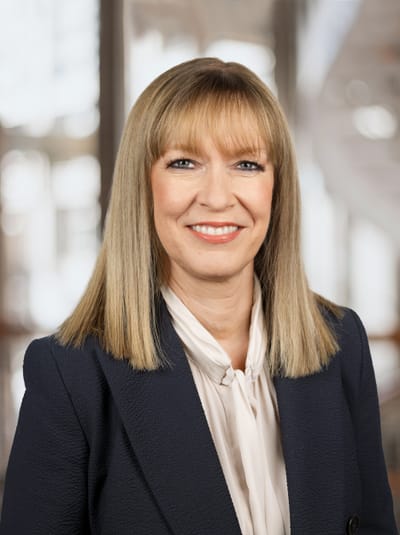 Frau in formeller Kleidung lächelt in Kamera.