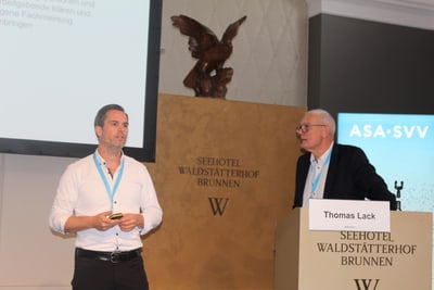 Zwei Männer auf einer Konferenzbühne mit Podium.