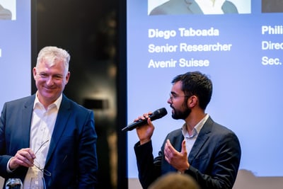 Zwei Männer auf einer Präsentation, einer spricht ins Mikrofon.