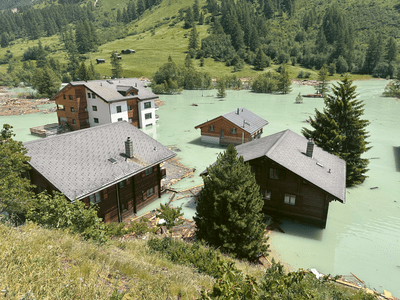 Überflutete Holzhäuser in einer grünen Berglandschaft.