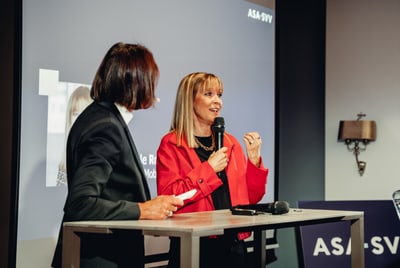 Zwei Personen sprechen auf einer Bühne bei einer Veranstaltung, eine Person hält ein Mikrofon.