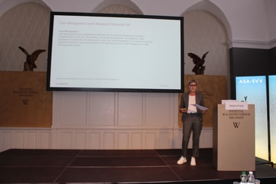 Person hält Vortrag vor einer Leinwand in einem Konferenzraum.