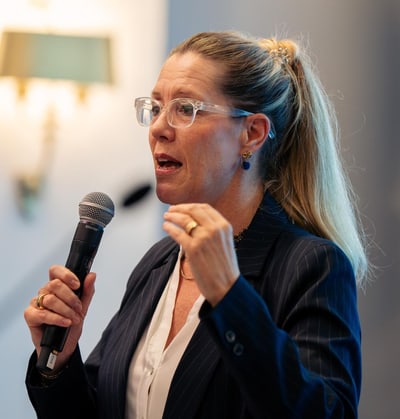 Femme avec lunettes tient un micro et parle.