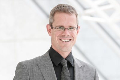 Person mit Brille im Anzug lächelt.