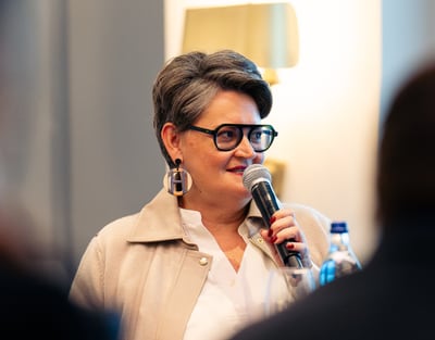 Person mit Mikrofon spricht lächelnd bei Veranstaltung.