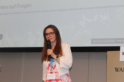 Person hält Mikrofon vor Projektionsleinwand.