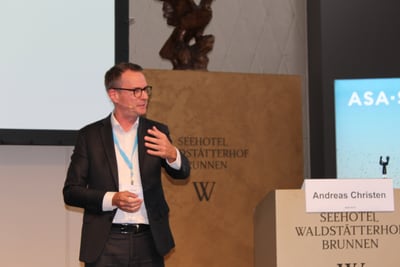 Mann in Anzug hält Vortrag vor Publikum.